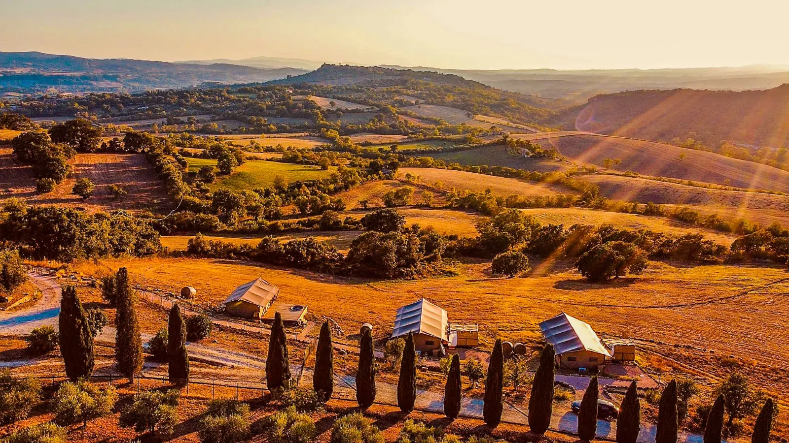 Rolling Italian hills at sunset with glamping tents among cypress trees